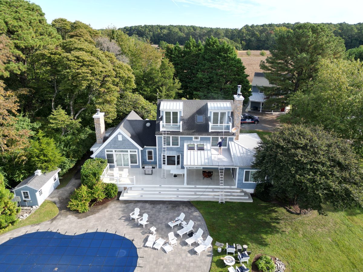 Wide aerial view of a blue coastal home, deck, pool patio and lawn during a full exterior soft wash by Coastal Shine